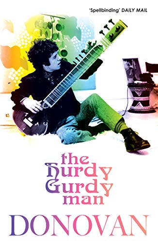 A man sits on the floor playing a sitar, with colorful abstract background graphics.