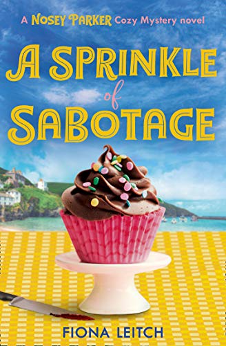 Book cover: cupcake, coastal scene, and title “A Sprinkle of Sabotage.”