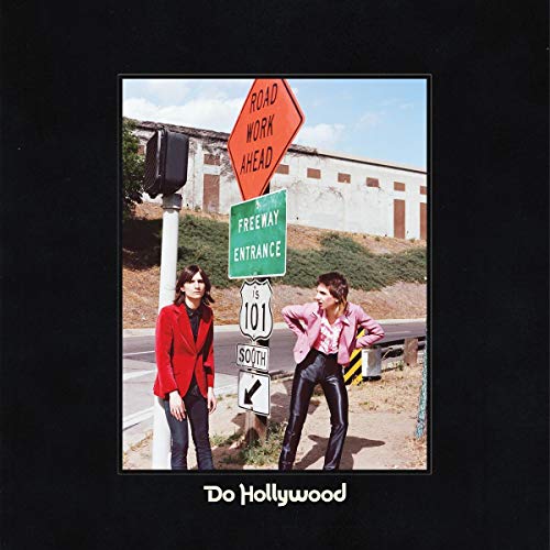 Two people stand near freeway signs and a concrete building.