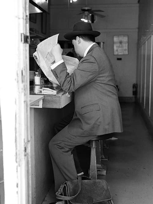 Man in suit reading a newspaper at a diner counter.