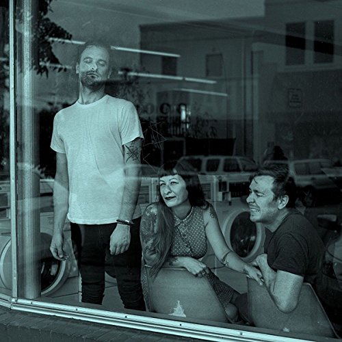 The image depicts a black-and-white photograph of three people visible through a window. For accessibility purposes, a suitable alt text could be: "Three people seen through a window, reflected on the glass."