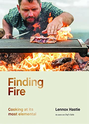 A chef cooks meat over an open fire on a grill.
