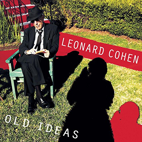 Leonard Cohen in a suit and hat sits on a chair in a garden.