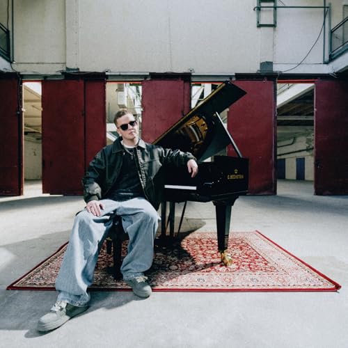 Man with sunglasses sits on a piano with a red rug.
