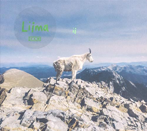 A mountain goat stands on a rocky summit with mountains in the background.