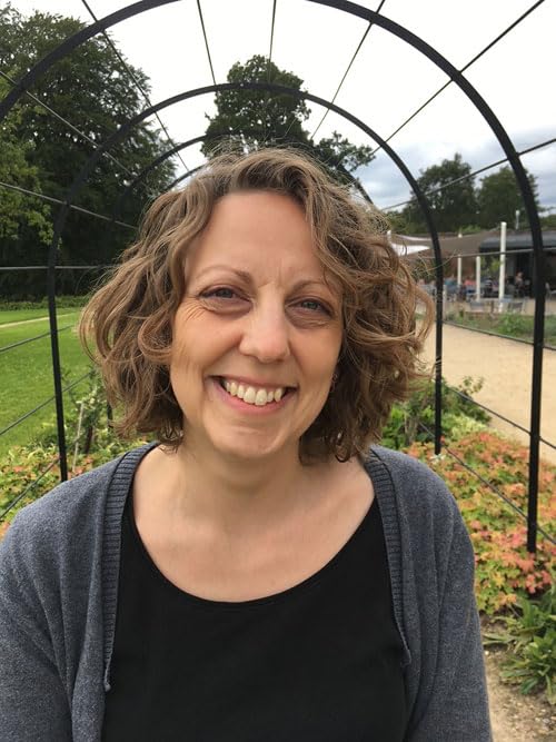 Woman with curly hair smiles under a metal garden archway.