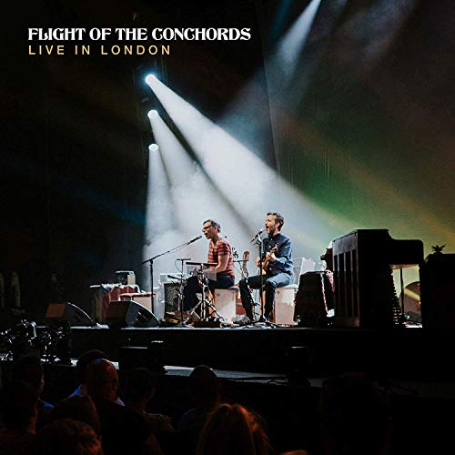 Flight of the Conchords performing live on stage with bright lights.