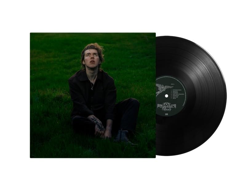 A man sits in a dark field next to a black vinyl record.