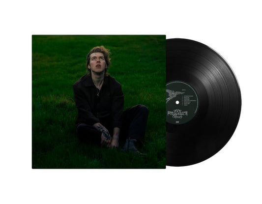 A man sits in a dark field next to a black vinyl record.