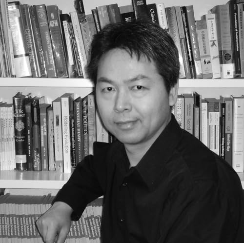 Black and white photo of a man sitting in front of a bookshelf.