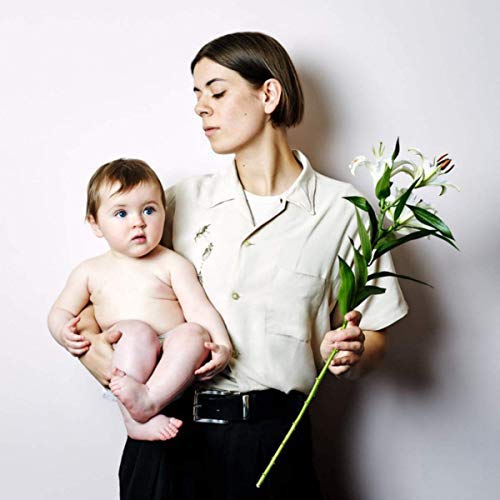 A woman holding a naked baby and a bouquet of white lilies.