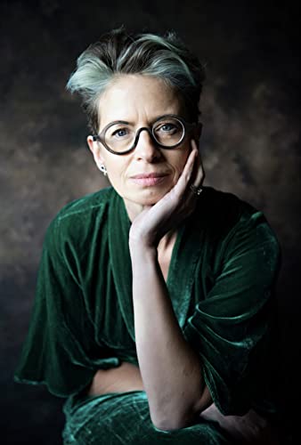 Woman with short gray hair and green velvet top resting her chin on her hand.