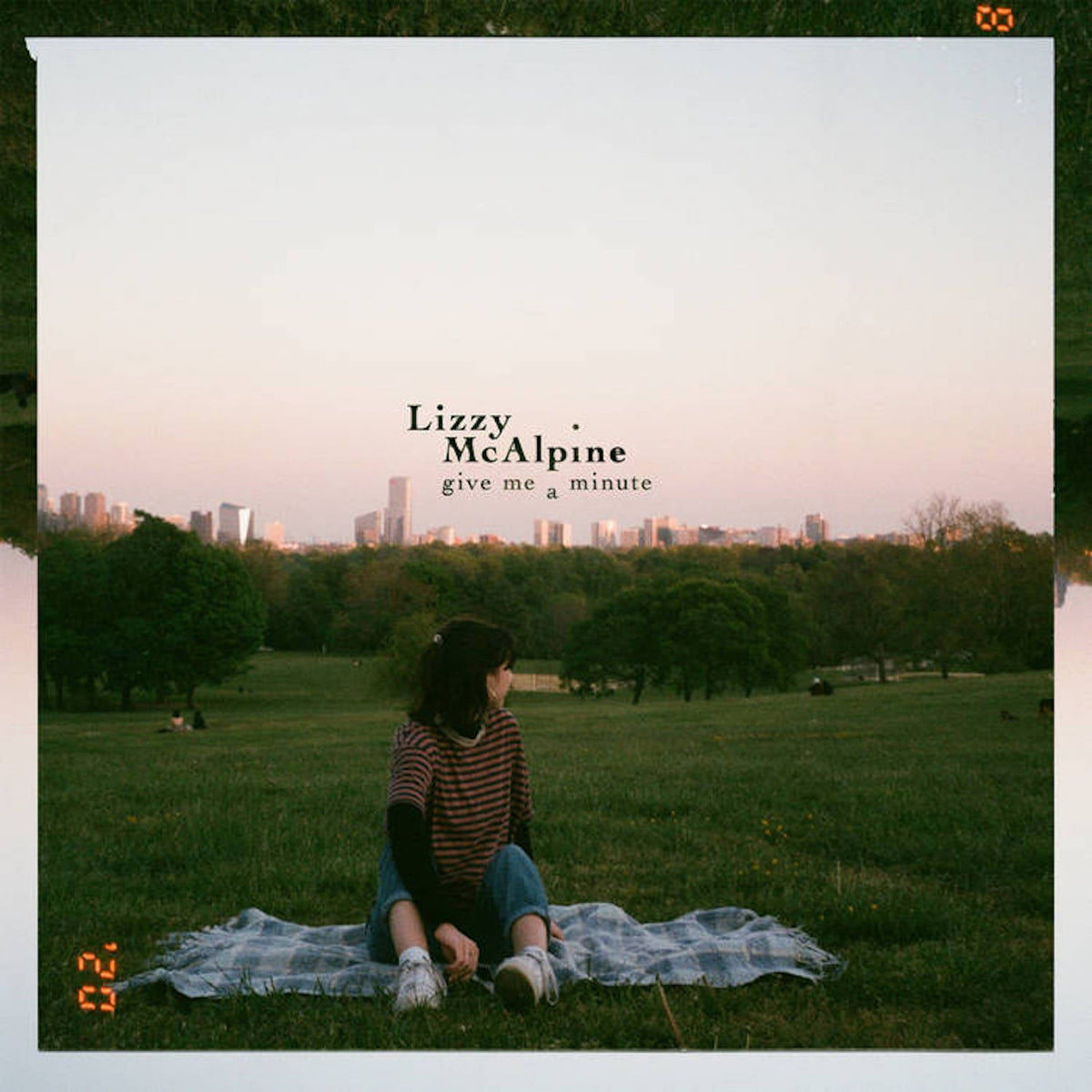 Album cover: Lizzy McAlpine sits in a field with a city skyline.
