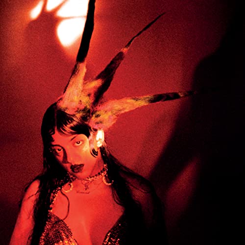 Woman with dark hair and feather-like headpiece in red lighting.