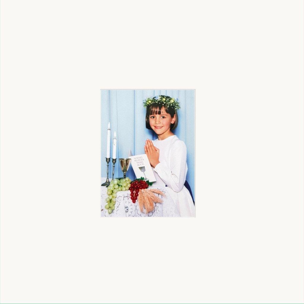 Girl in white dress with flower crown, praying at altar.