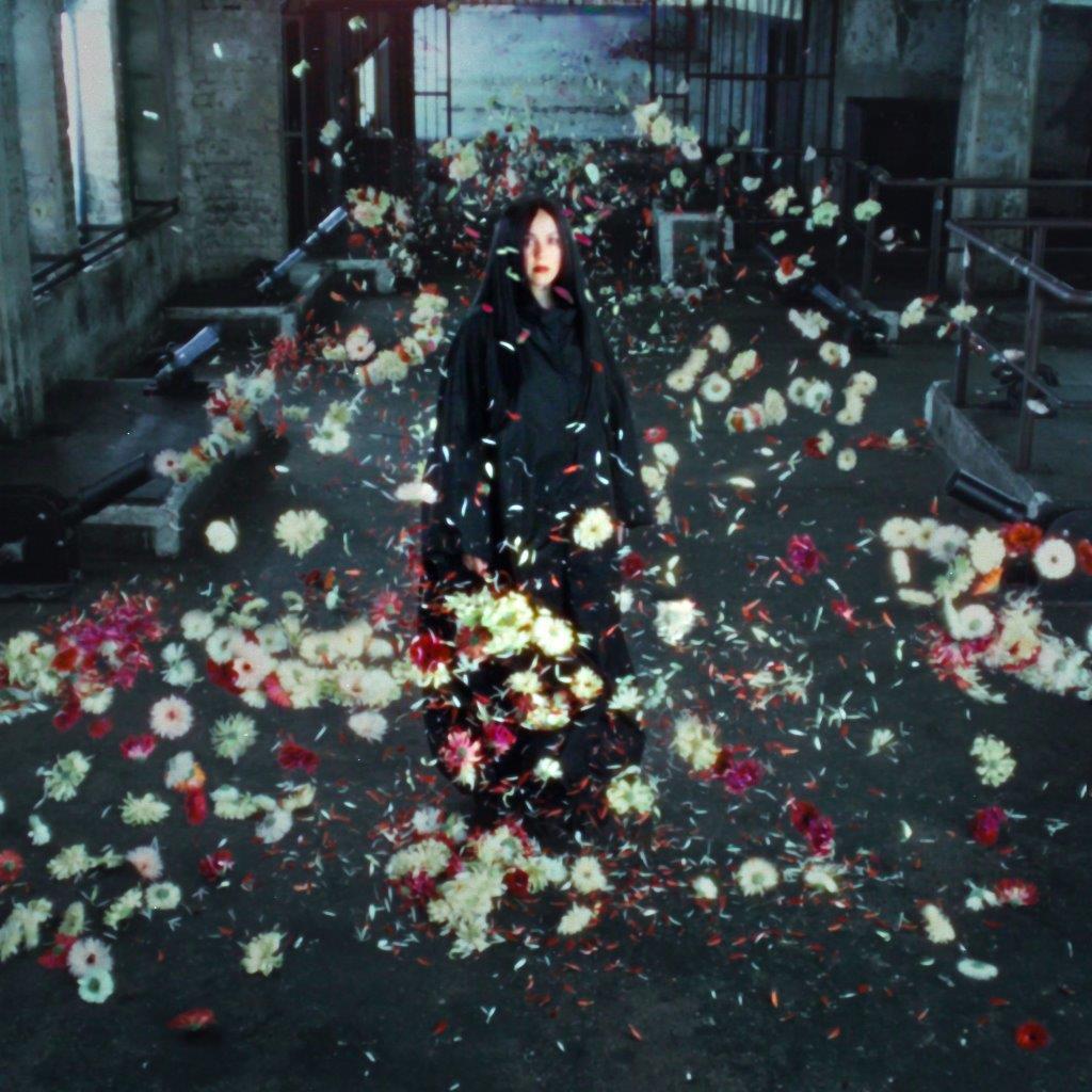 Woman in black coat surrounded by falling white and red flowers.