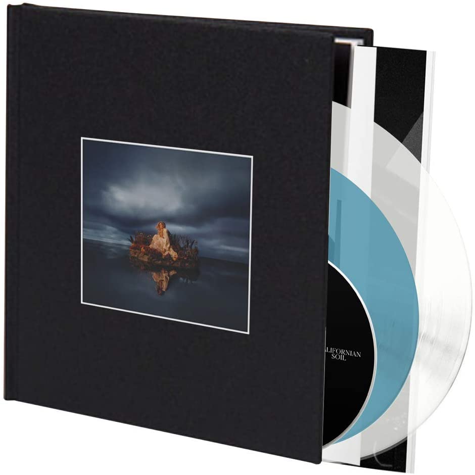 Album cover: woman in white dress on a small island, stormy sky.