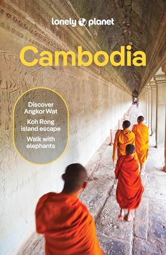 Monks in orange robes walk through a stone corridor with carved walls at Angkor Wat.