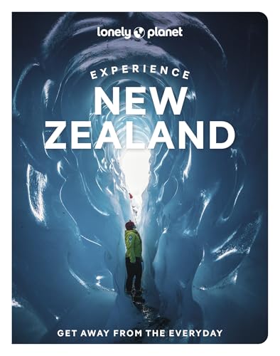 A person in a green jacket stands inside a deep blue glacier ice cave.
