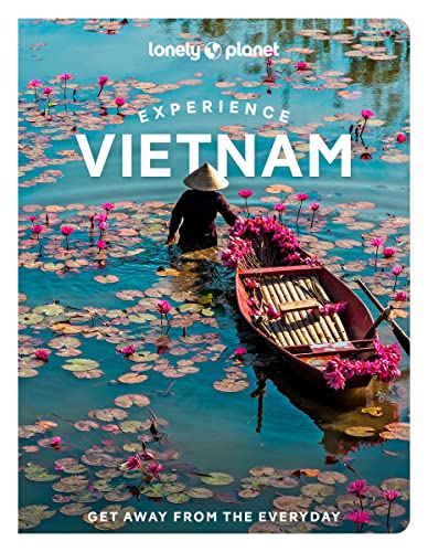 A person in a conical hat stands in a boat amidst pink water lilies.