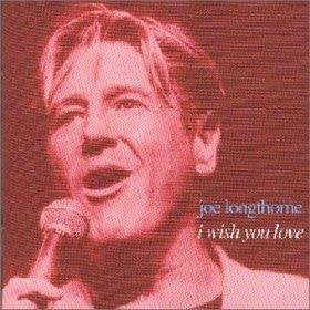 Close-up of Joe Longthorne singing into a microphone, red background.