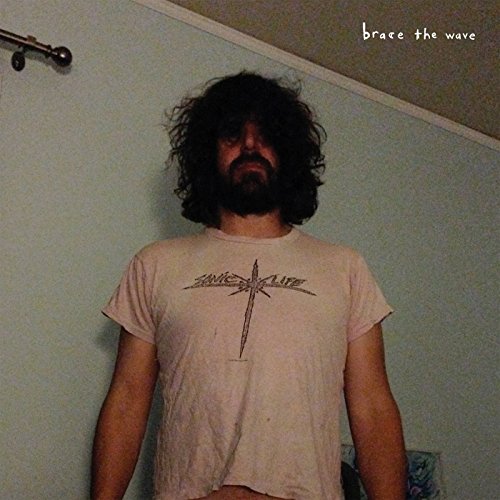 Lou Barlow with messy hair wearing a Sonic Life t-shirt against a light wall.