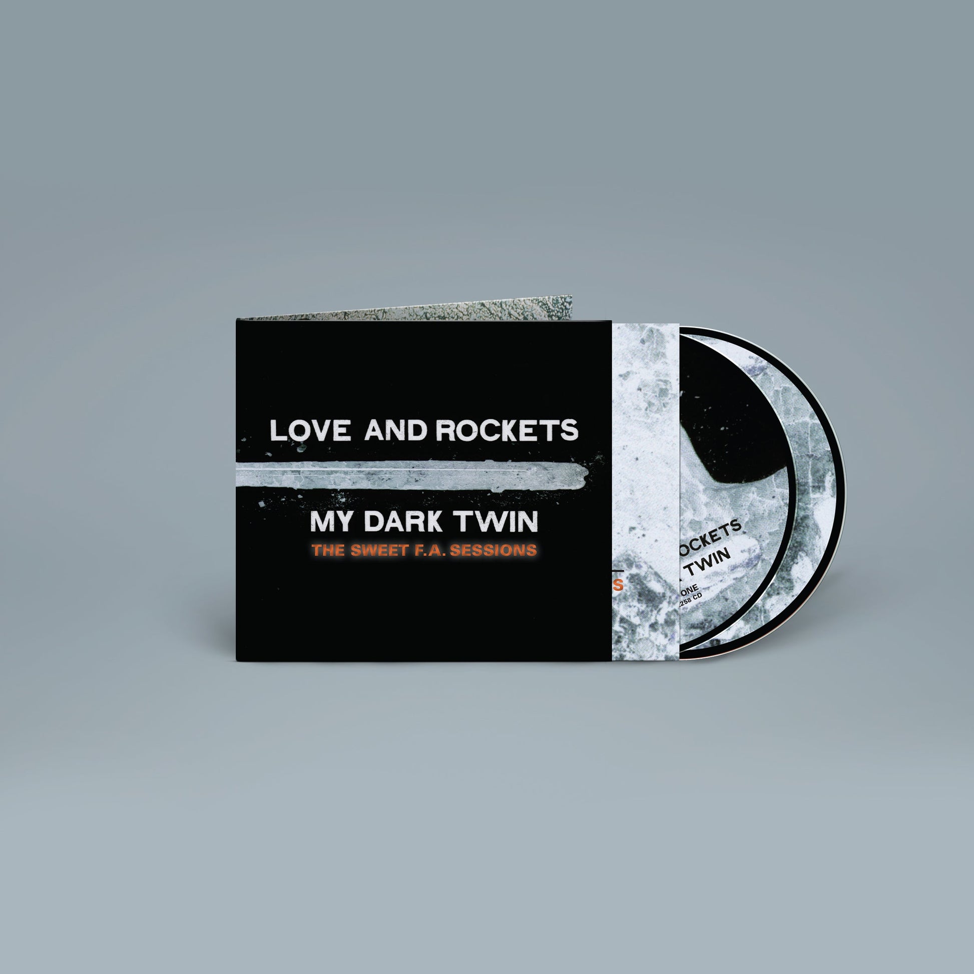 "CD case with two discs, black cover with white and orange text, grey background."
