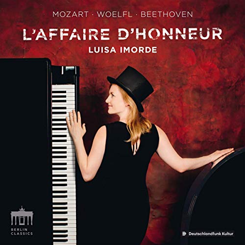 A woman in a black dress and hat stands beside a piano against a red background.