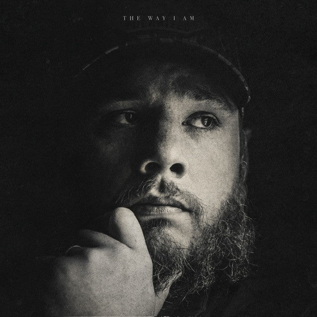 Black and white portrait of Luke Combs with beard, looking upwards.
