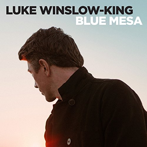 "Album cover featuring a man in a dark coat with head bowed, against a gradient background."