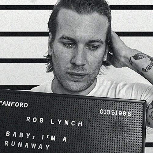 "Black and white mugshot of Rob Lynch with a sign displaying album title and artist."