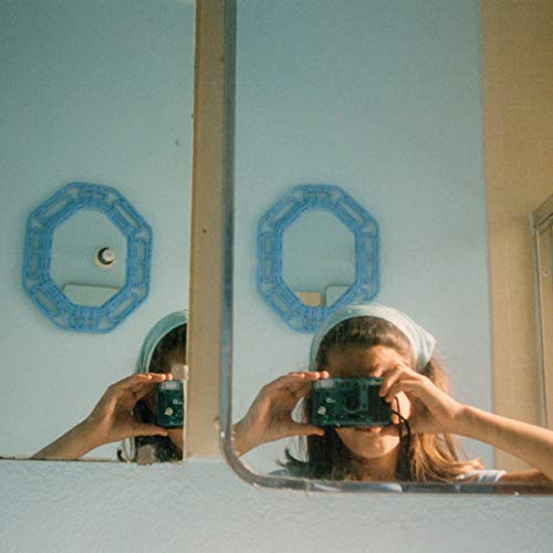 Woman in headscarf holding a camera up to her face, reflected in mirrors.