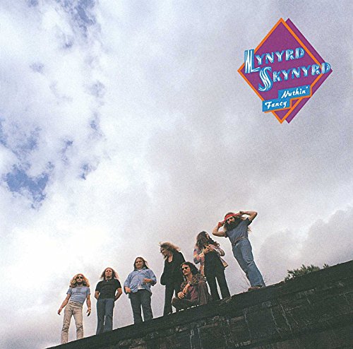 Lynyrd Skynyrd band members standing on a ledge against a cloudy sky.