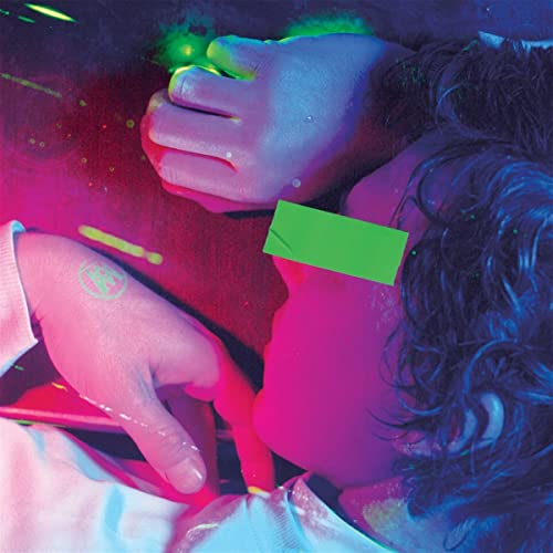 Person with a green rectangle over their eyes, illuminated by magenta and blue light.