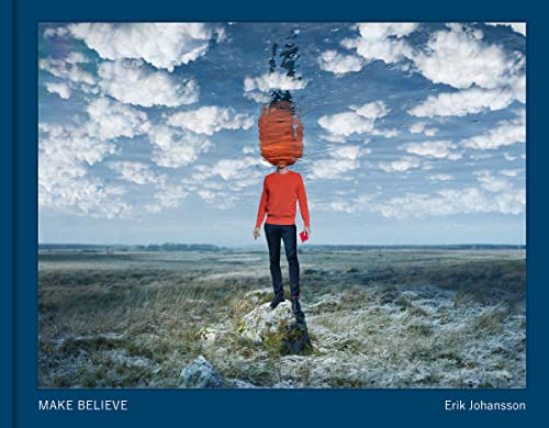 A person in a red sweater stands on a rock beneath a mirrored cloudy sky.