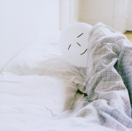 White balloon with a drawn face rests on rumpled bedding.