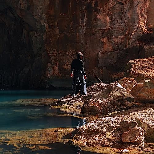 Person standing on rocks inside a dimly lit cave overlooking water.