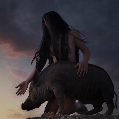 A person with long dark hair kneeling beside a pig against a cloudy sky.