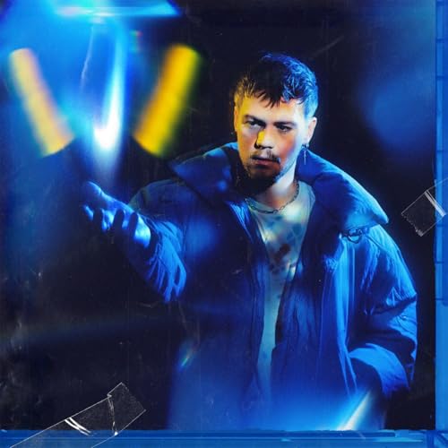 A man in a blue jacket reaches forward under bright blue and yellow lighting.