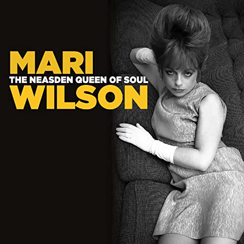 Black and white photo of Mari Wilson with beehive hair, wearing gloves and dress.