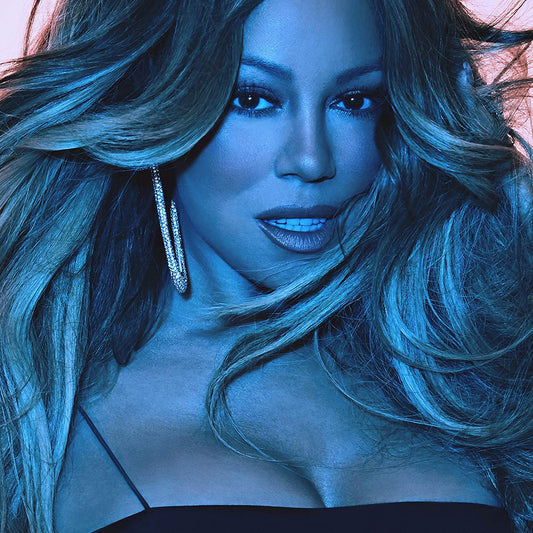 Mariah Carey in a black top, with flowing hair, against a pink background.