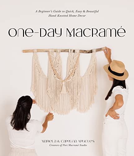 Two women hanging a large cream-colored macrame wall hanging on a white wall.