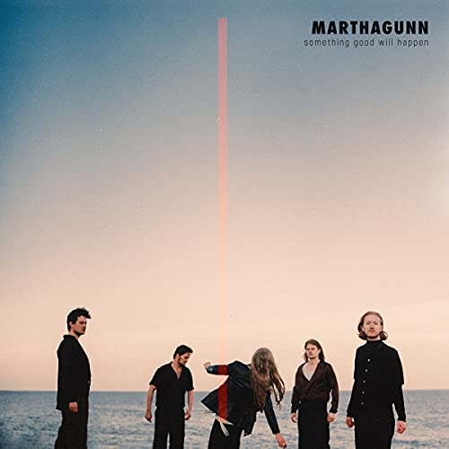 Five people in black clothing standing by the ocean with a red laser beam.