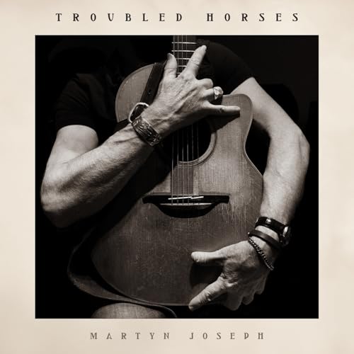 Close-up of a man embracing an acoustic guitar, album cover.