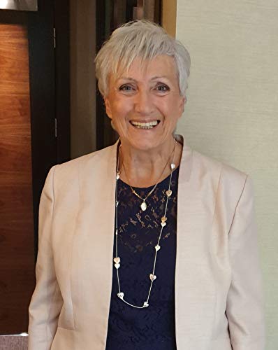 Close-up of a smiling older woman in a blazer and necklace.