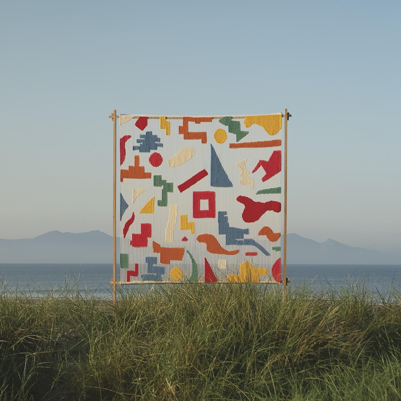Woven textile with abstract shapes displayed outdoors near the sea.