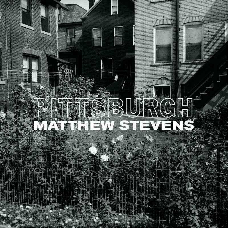 Black and white photo of city houses behind a fence with text overlay.