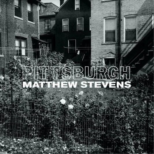 Black and white photo of city houses behind a fence with text overlay.