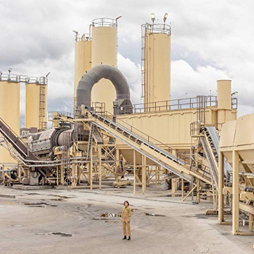 Woman stands small before a large industrial factory complex.