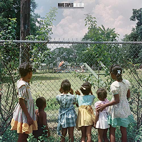 Five children stand behind a chain-link fence looking at a distant fairground.